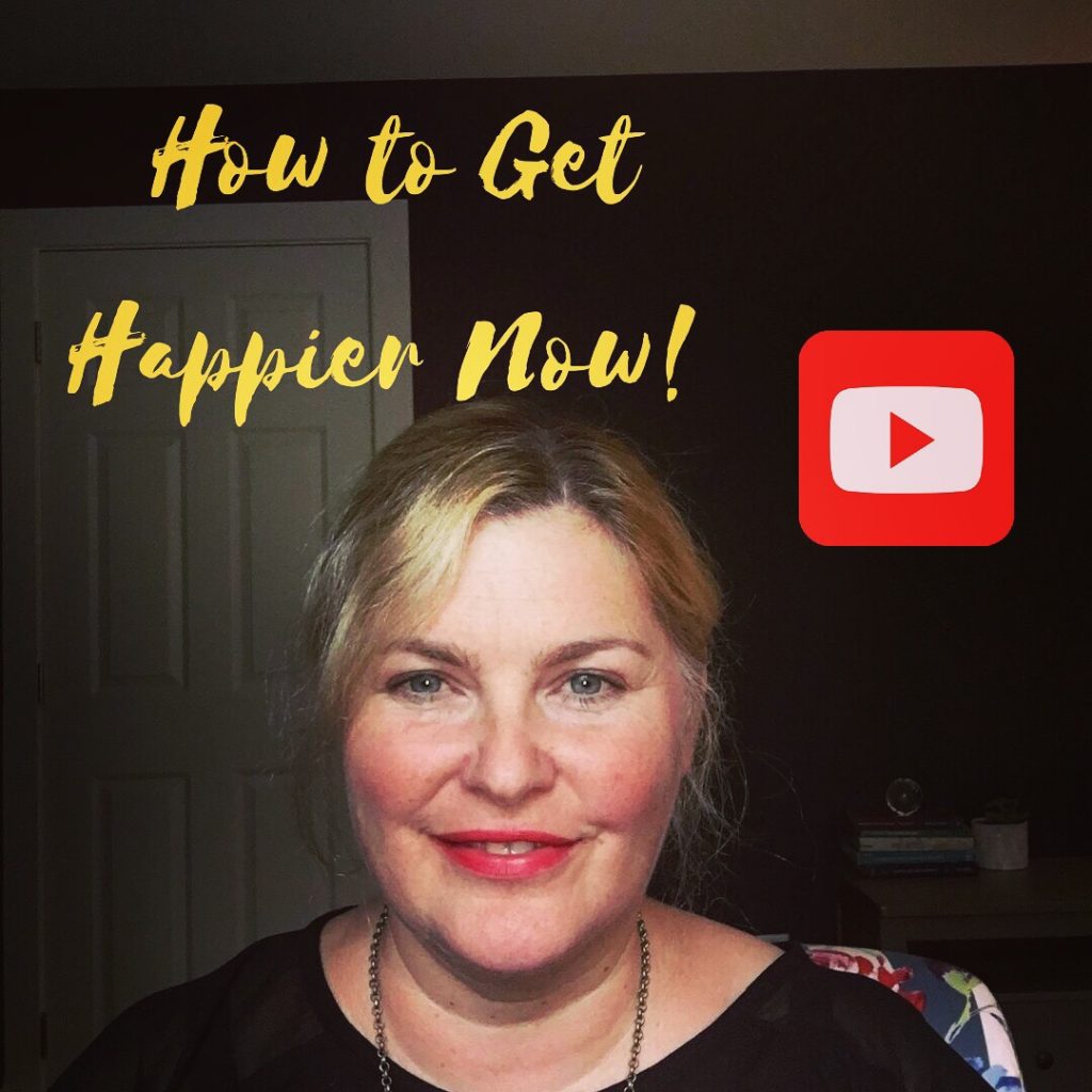 In the picture Elizabeth is smiling at the camera, she is wearing a black top and necklace. behind her is a white door and dark blue wall. The picture reads 'How to Get Happier Now' and there is a red and white YouTube emblem next to her head.